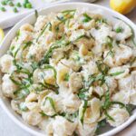 white bowl with ricotta pasta and peas topped with parmesan and basil.