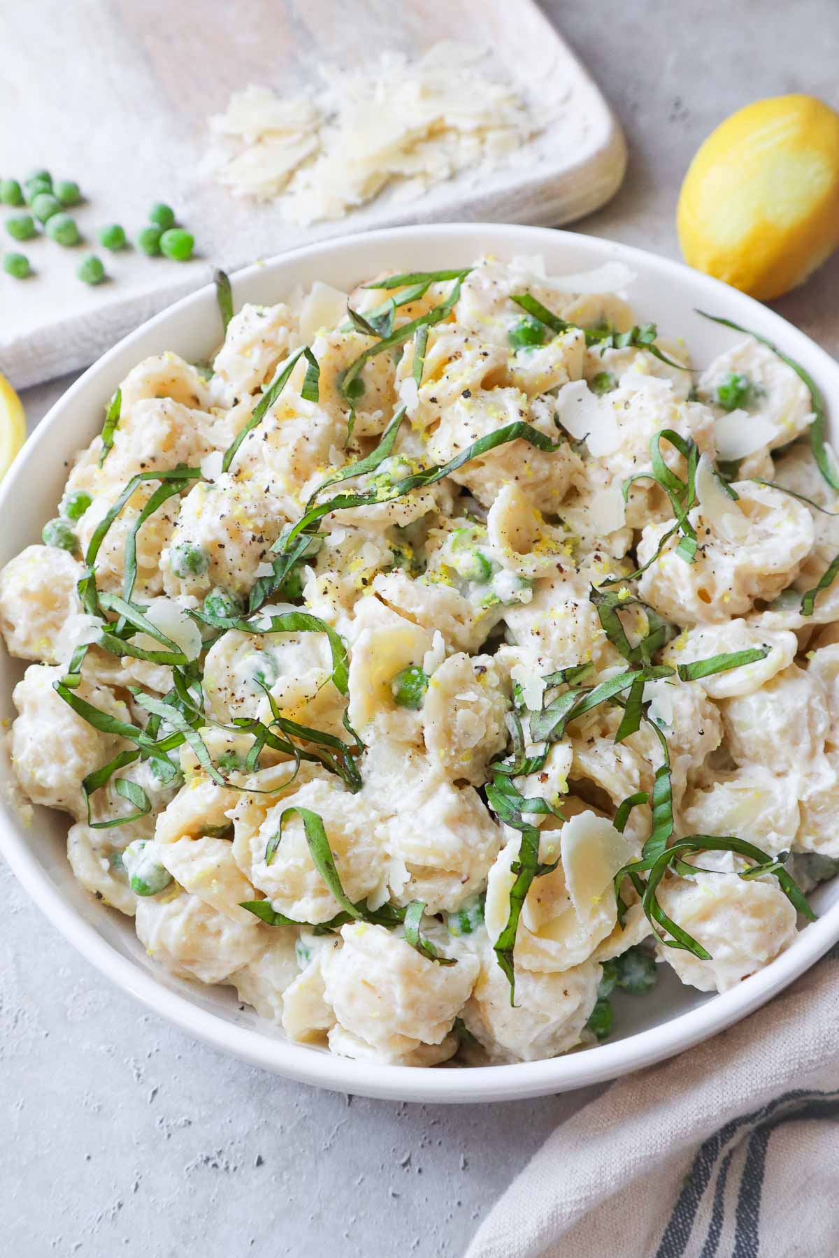 white bowl with ricotta pasta and peas topped with parmesan and basil.