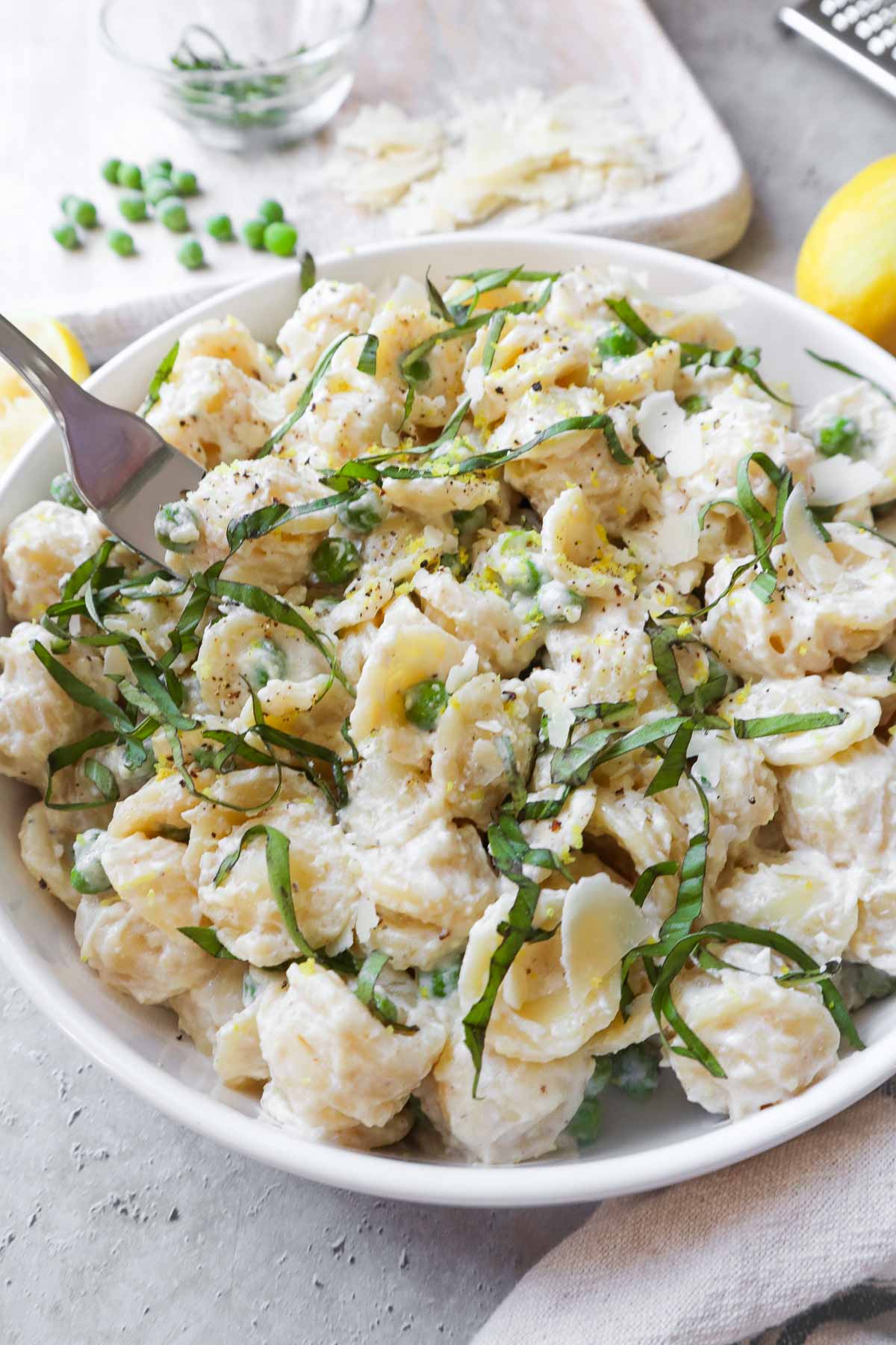 white bowl with ricotta pasta and peas topped with parmesan and basil.