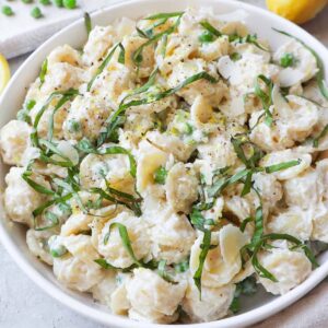 white bowl with ricotta pasta and peas topped with parmesan and basil.
