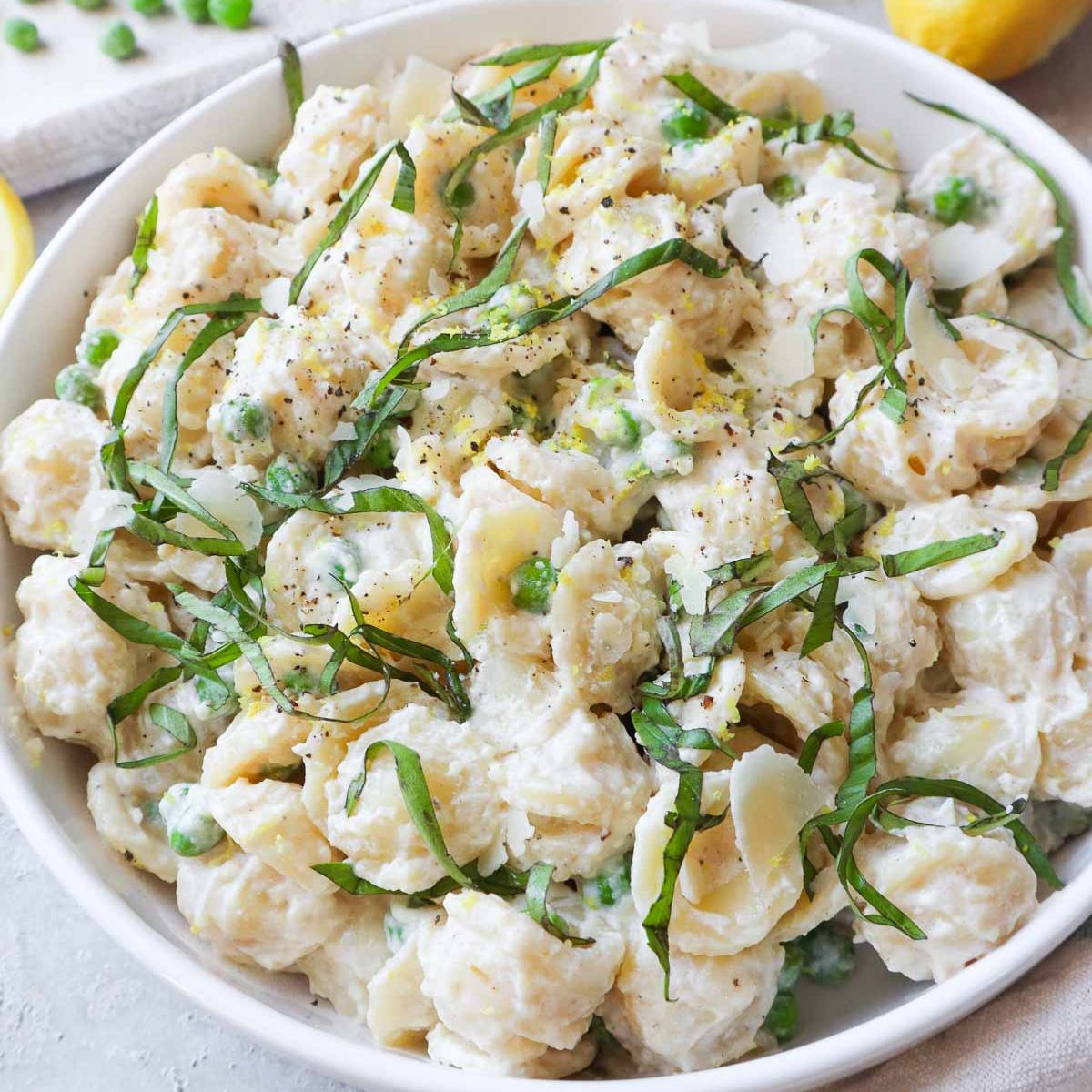 white bowl with ricotta pasta and peas topped with parmesan and basil.