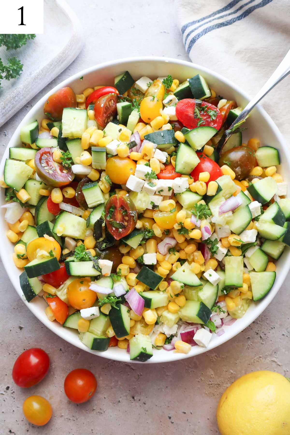 white bowl with mixed ingredients to make tomato corn cucumber salad mixed together without seasonings.