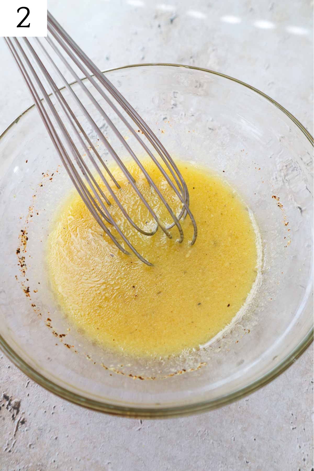 glass bowl with dressing ingredients whisked together.