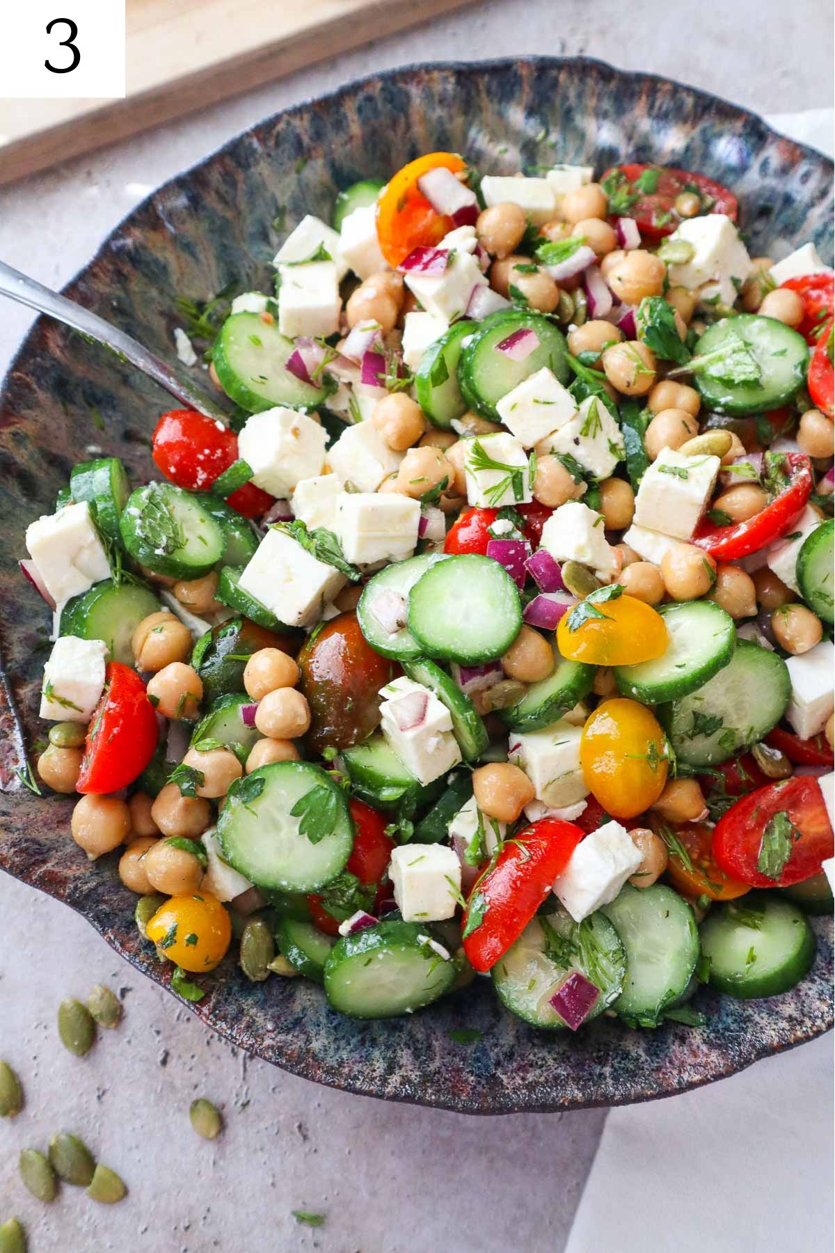 bowl with cucumber chickpea feta salad with spoon.