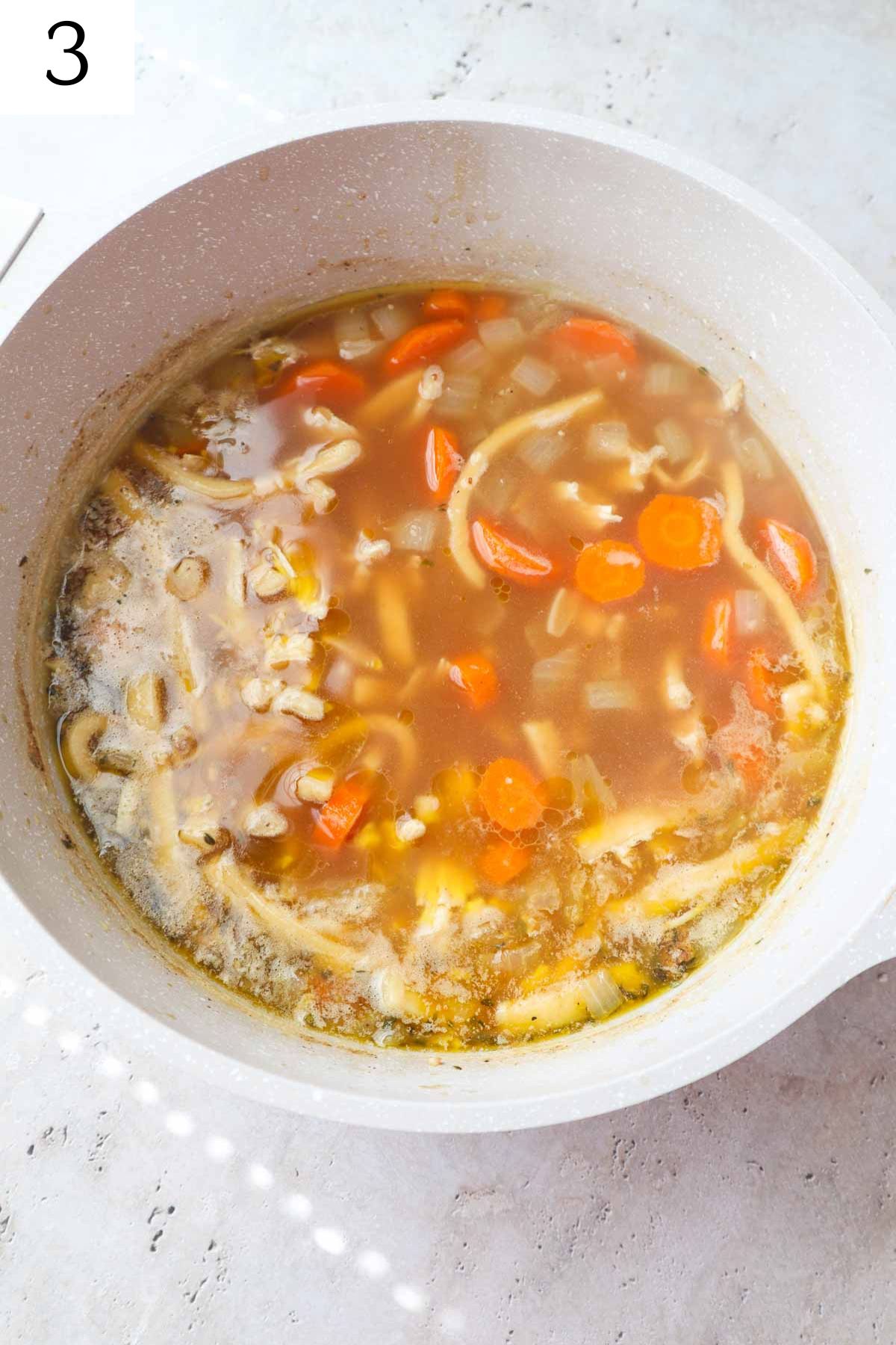 pot with noodles, carrots, onion, and chicken broth.