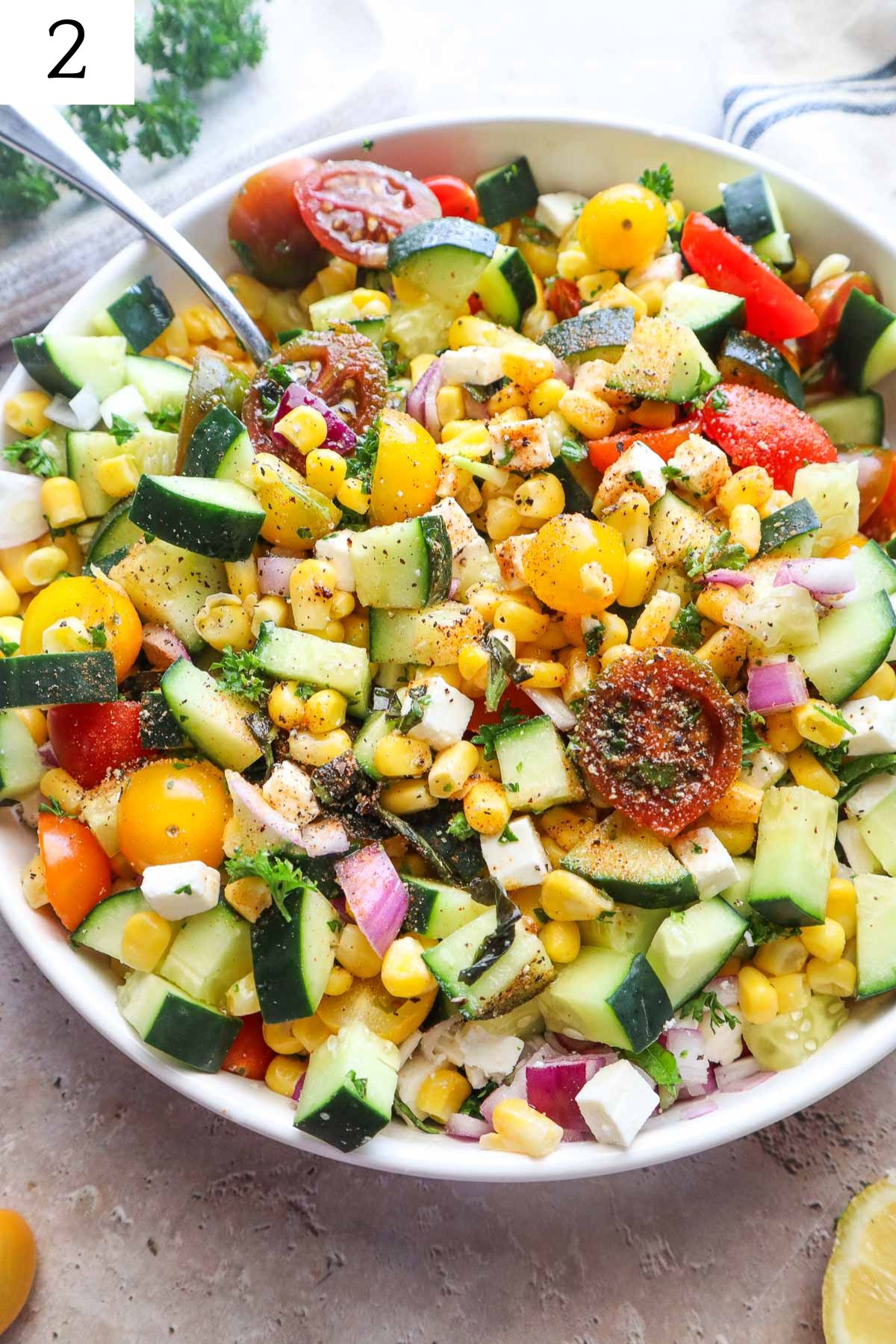 all ingredients to make tomato corn cucumber salad in a bowl all mixed together with seasonings.