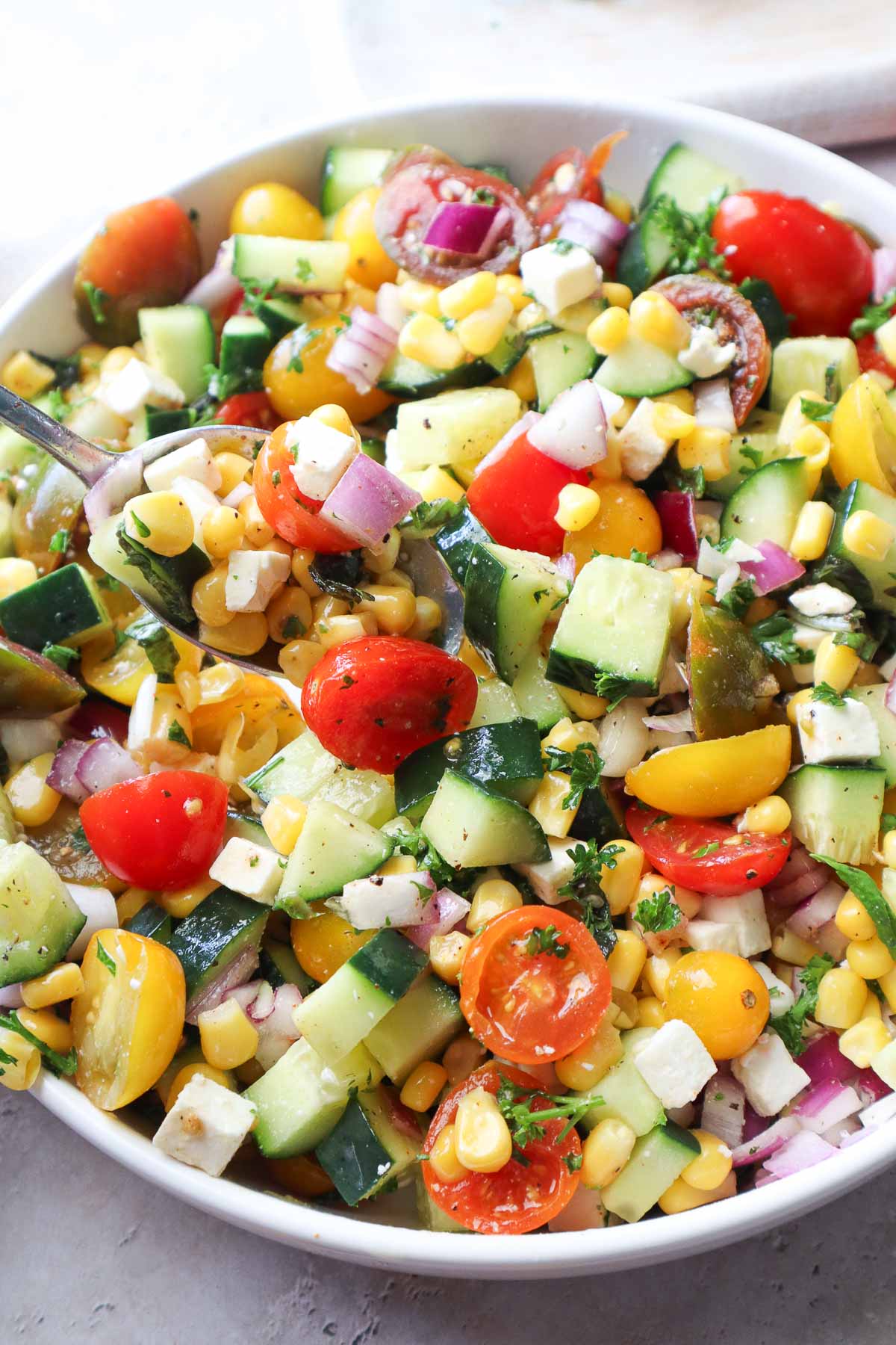 bowl with tomato corn cucumber salad tossed in lemon juice and olive oil.