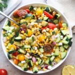 bowl with tomato corn cucumber salad tossed in lemon juice and olive oil.