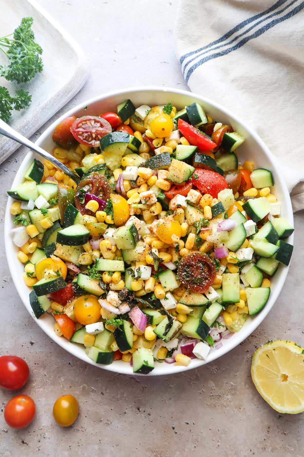 bowl with tomato corn cucumber salad tossed in lemon juice and olive oil.