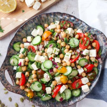 bowl with cucumber chickpea feta salad topped with various herbs and tossed in the dressing.