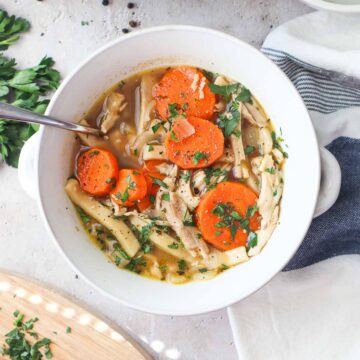 bowl with chicken noodle soup without celery topped with parsley.