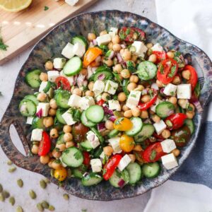bowl with cucumber chickpea feta salad topped with various herbs and tossed in the dressing.