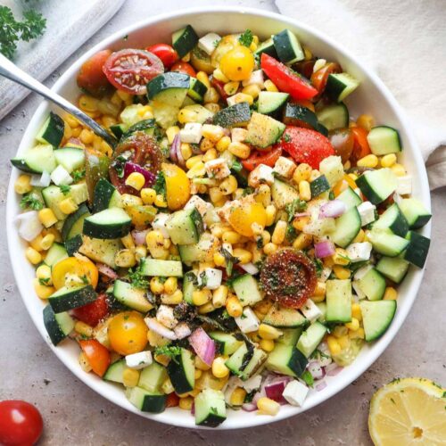 bowl with tomato corn cucumber salad tossed in lemon juice and olive oil.