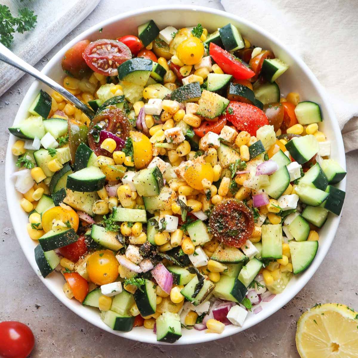 bowl with tomato corn cucumber salad tossed in lemon juice and olive oil.