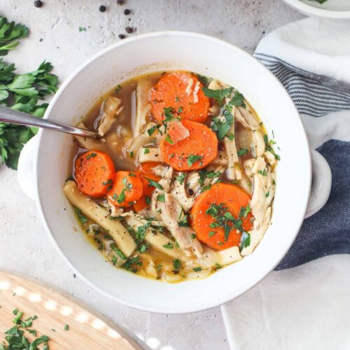bowl with chicken noodle soup without celery topped with parsley.