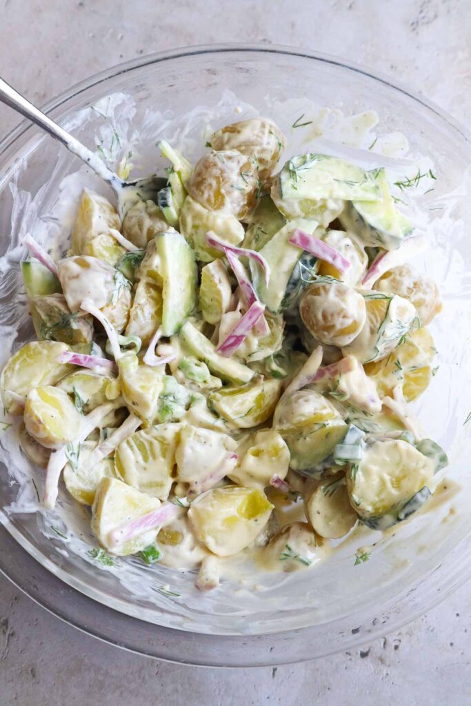 glass bowl with all ingredients to make potato salad mixed together and coated evenly with the dressing.