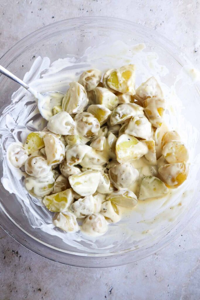 glass bowl with warm potatoes mixed into the dressing.