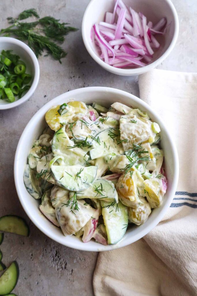 glass bowl with potato salad and cucumbers topped with fresh dill.