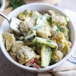 glass bowl with potato salad and cucumbers topped with fresh dill.