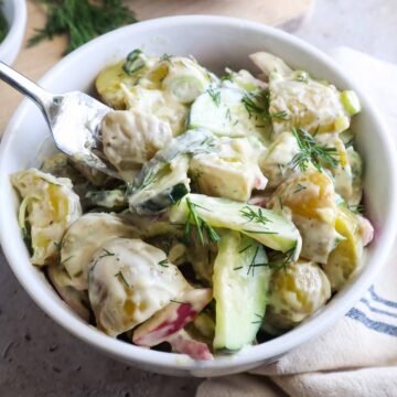 glass bowl with potato salad and cucumbers topped with fresh dill.