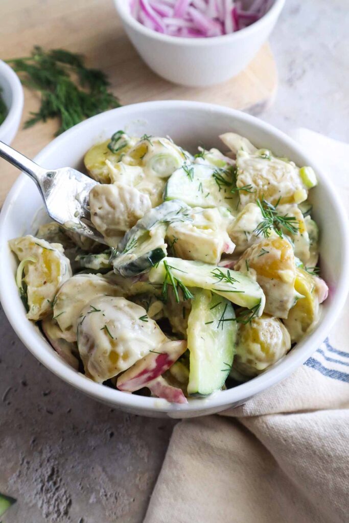 glass bowl with potato salad and cucumbers topped with fresh dill.