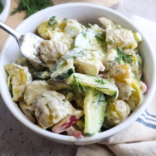 glass bowl with potato salad and cucumbers topped with fresh dill.