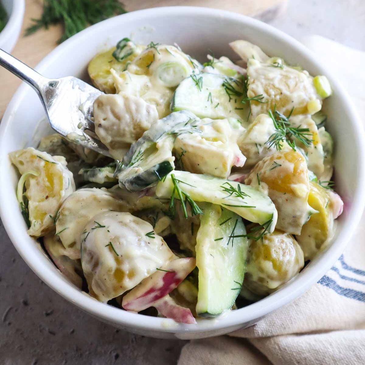 glass bowl with potato salad and cucumbers topped with fresh dill.