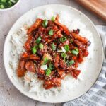 bourbon chicken over white rice topped with sesame seeds and green onion.