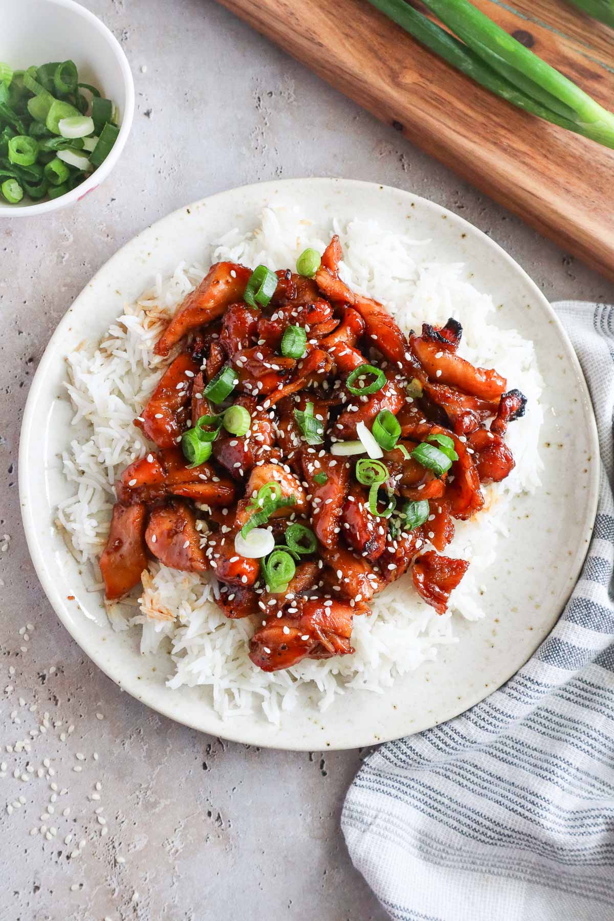 bourbon chicken over white rice topped with sesame seeds and green onion.