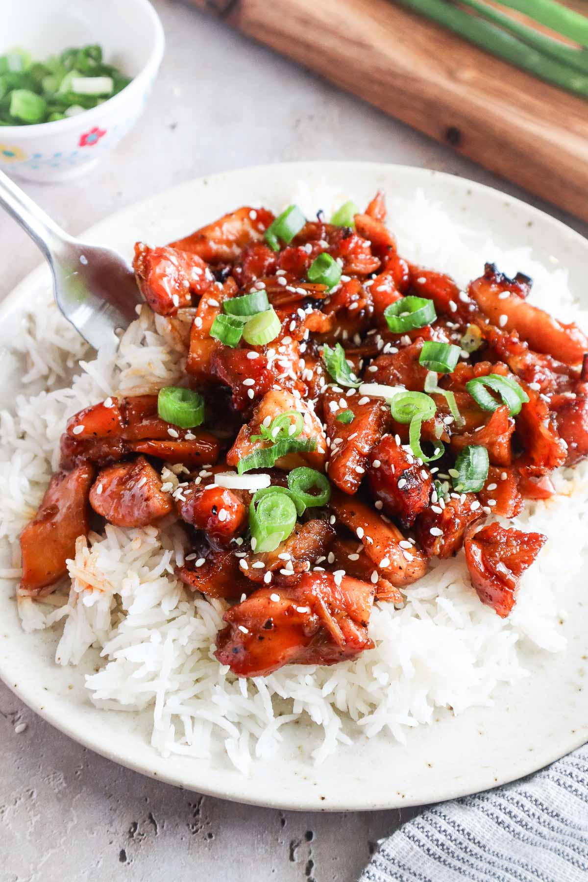 bourbon chicken over white rice topped with sesame seeds and green onion.