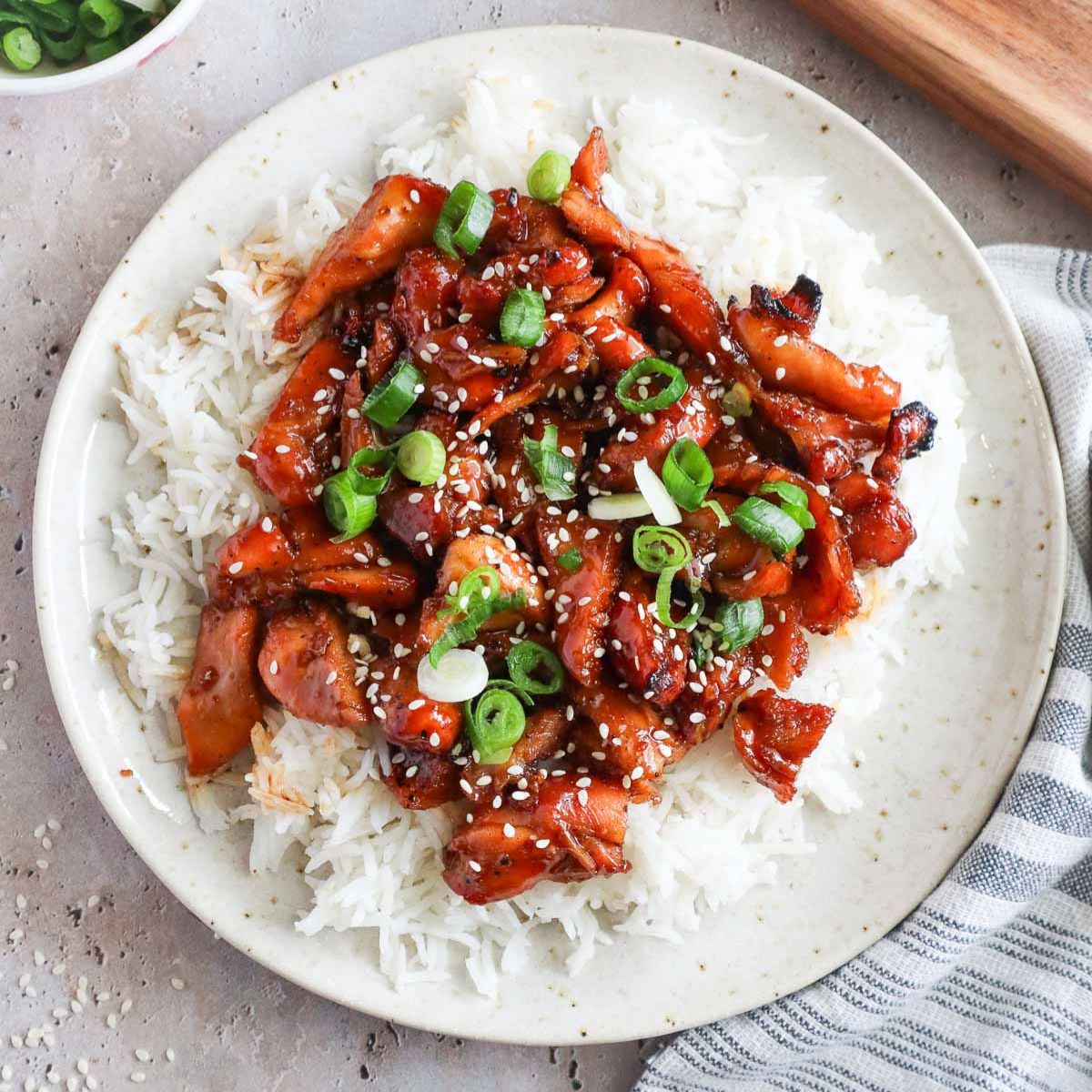 bourbon chicken over white rice topped with sesame seeds and green onion.
