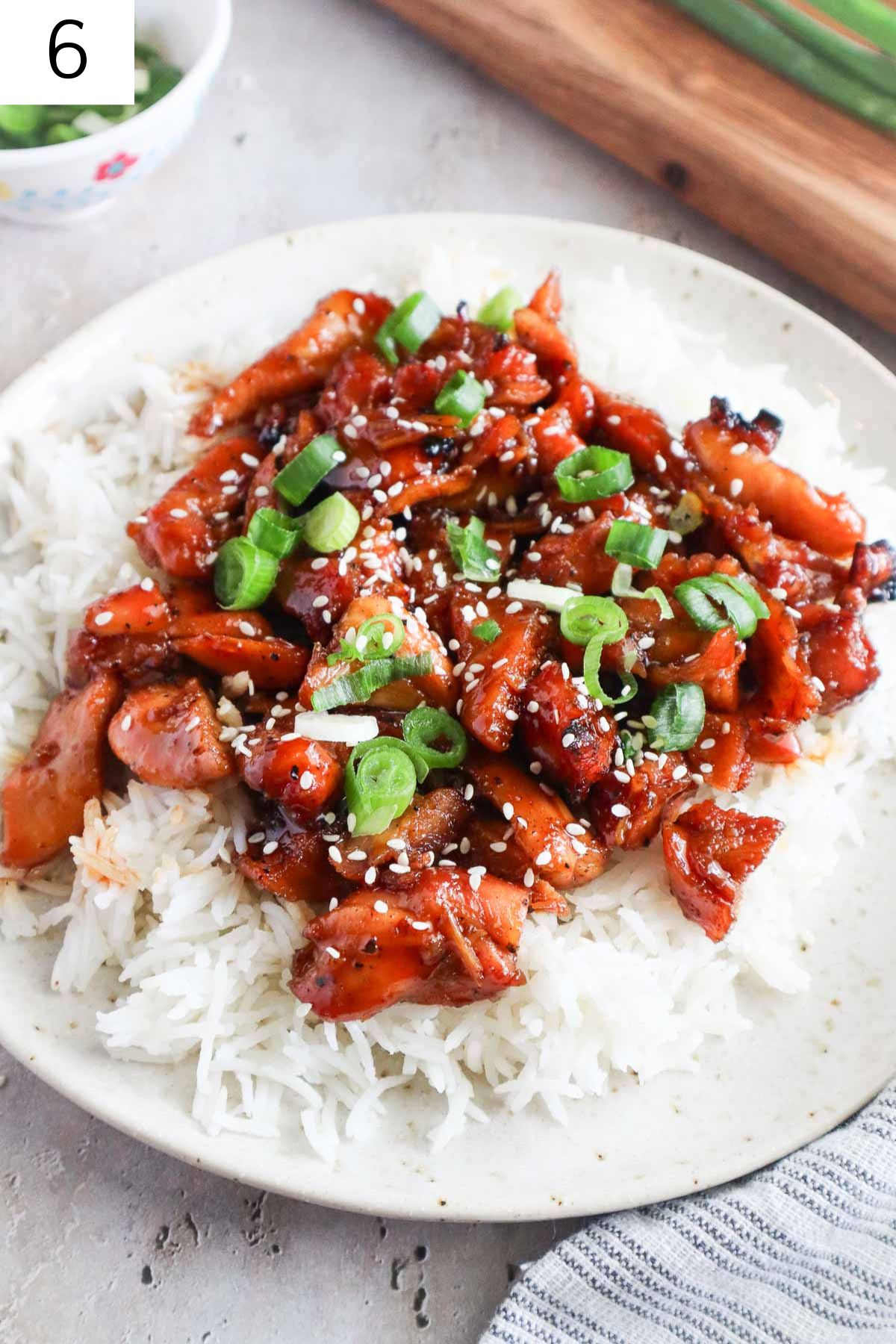 bourbon chicken over white rice topped with sesame seeds and green onion.