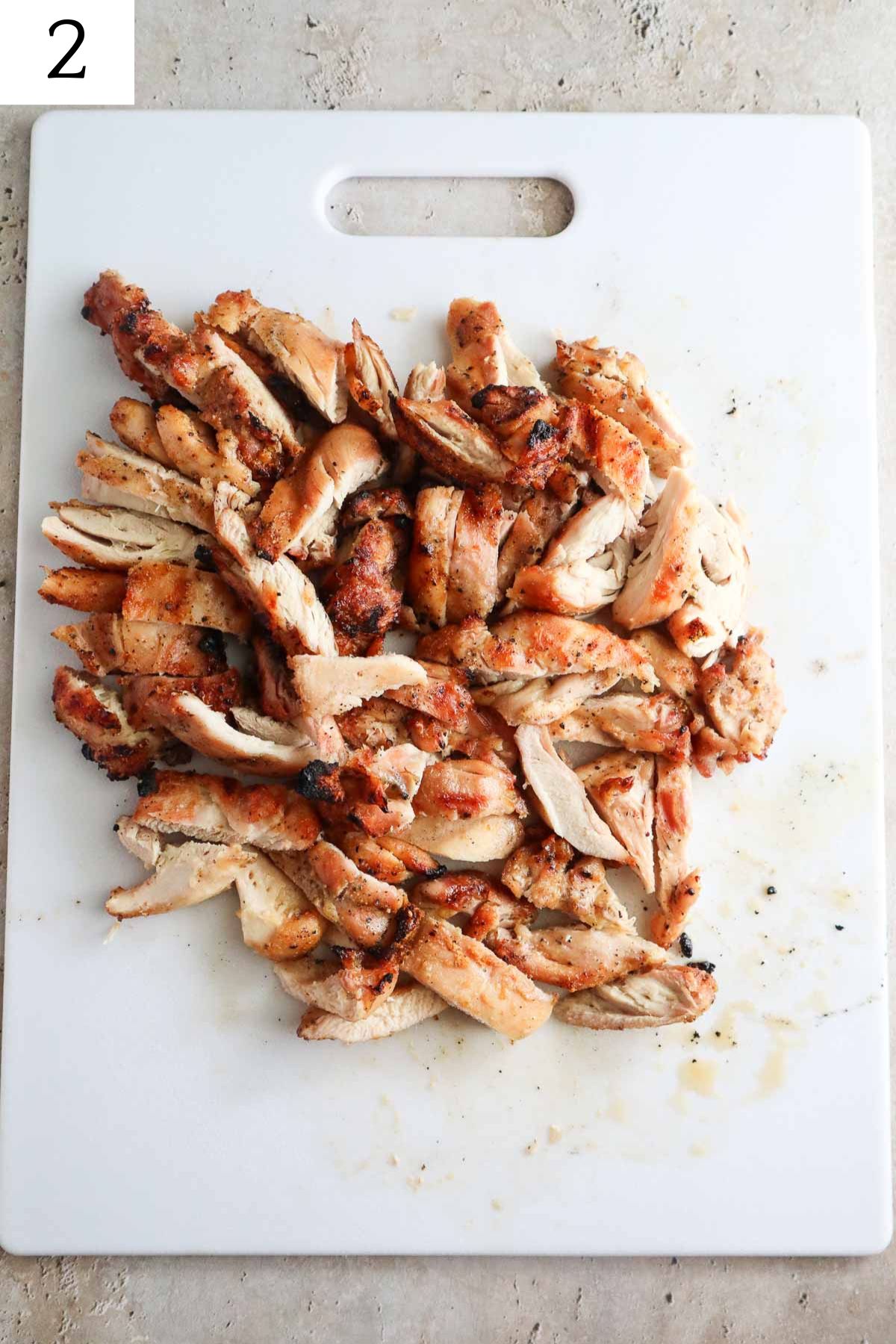 cutting board with seasoned grilled chicken chopped into slices.