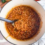dutch oven with spoon scooping maple baked beans.