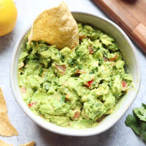 glass bowl with guacamole without onion and a chip dipping into it.